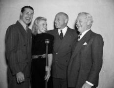 Cecil B. DeMille Posing With Actors at CBS Microphone